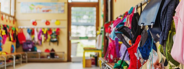 Leerer Flur in der Schule, Rucksäcke und Taschen an Haken, heller Aufenthaltsraum