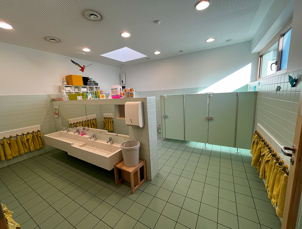 Großes, helles Badezimmer mit zwei Waschbecken, grünen Fliesen, gelben Handtüchern und Fenstern.