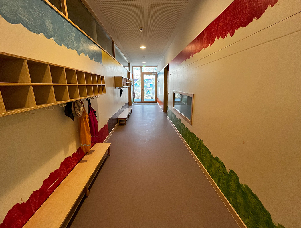 Ein leerer Flur mit bunten Wandmalereien und Holzbänken.