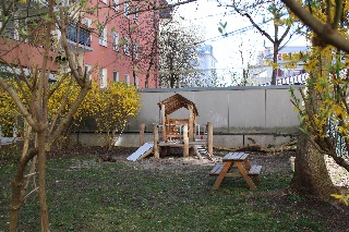 Ein leerer Spielplatz mit Holztisch, Rutsche und karger Vegetation im städtischen Hinterhof.
