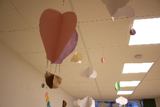 Papierwolken und farbige Herzen hängen von einer weißen Decke in einem hellen Raum.
