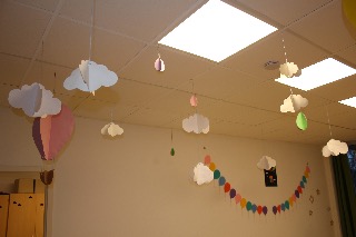 Papierwolken und Luftballons an der Decke eines Raumes, bunte Lichter und Dekorationen.
