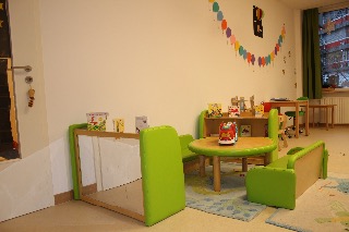 Kinderzimmer mit grünen Möbeln, runden Tisch, bunten Wänden und Büchern auf einem Regal.