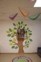 Raum mit farbenfroher Blattmalerei und Büchern auf Wandregal, bunte Wimpel an der Decke.