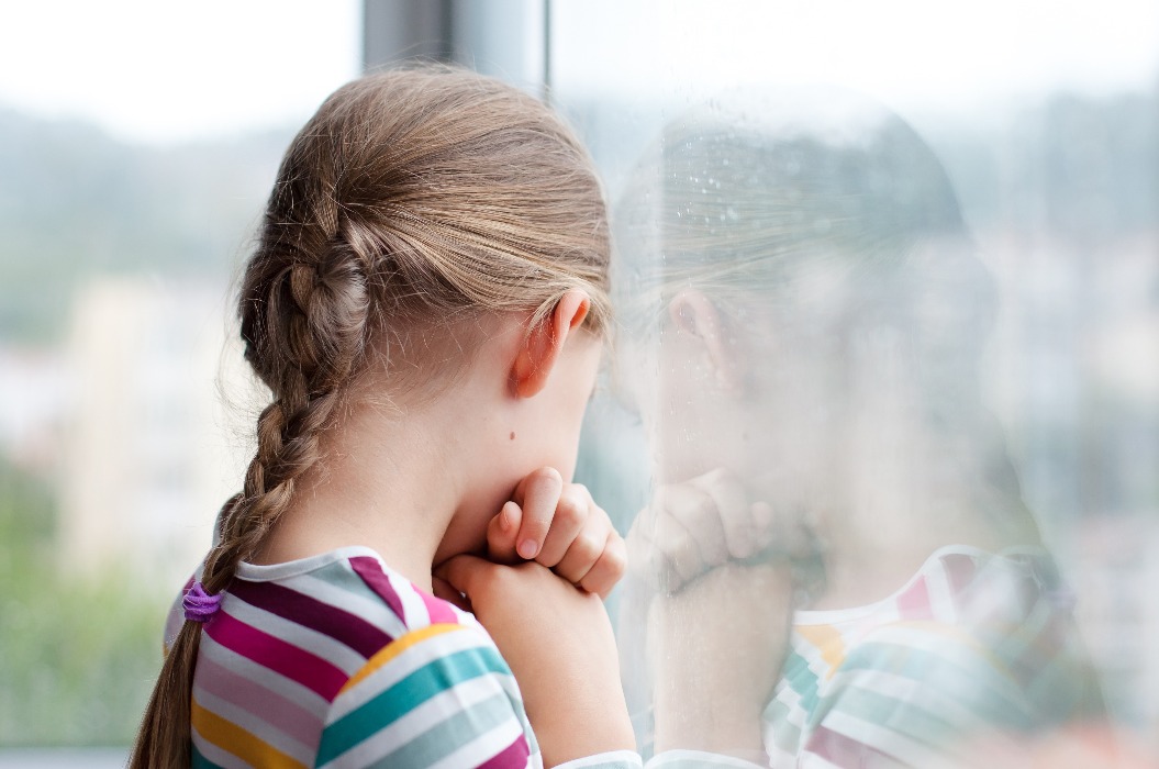 Trauriges Kind schaut durch ein verregnetes Fenster zu Hause. Aufgeregtes Kind in Selbstisolierung während der Quarantäne.